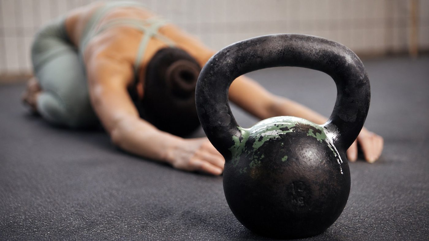 Kvinna stretchar bredvid en kettlebell i gymmet